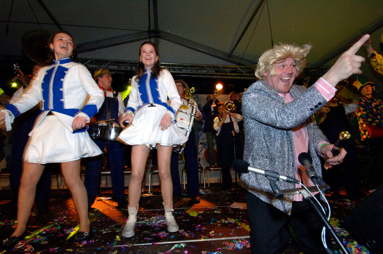 Kleurenfoto uit 2008: John Plegt met blonde pruik en glitterjasje zet het Oldenzaalse Kapellenfestival op de kop, met dansmarietjes en blazers.