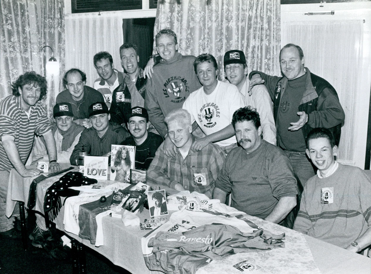 Zwart-witfoto uit 1995: de jonge Les Miezerables rond een tafel met bandshirts, lol en ondeugende spullen.